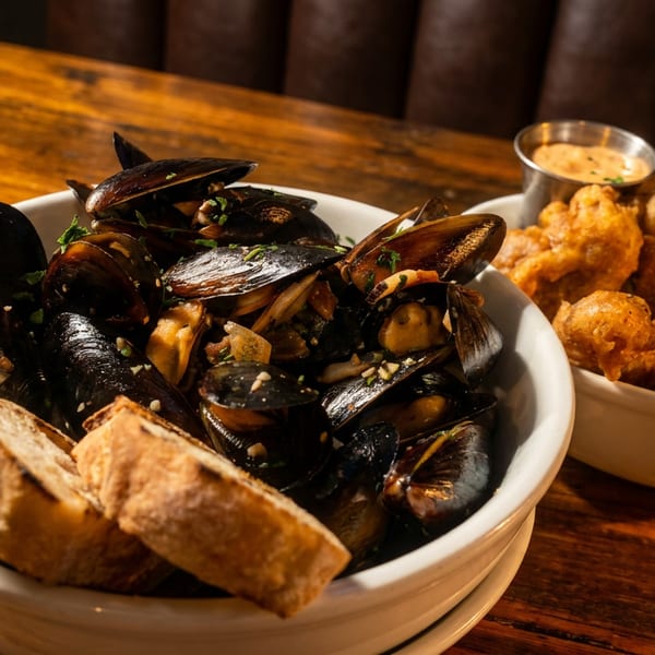 Steamed mussels with grilled bread and a bowl of fried calamari with dipping sauce on a wooden table.