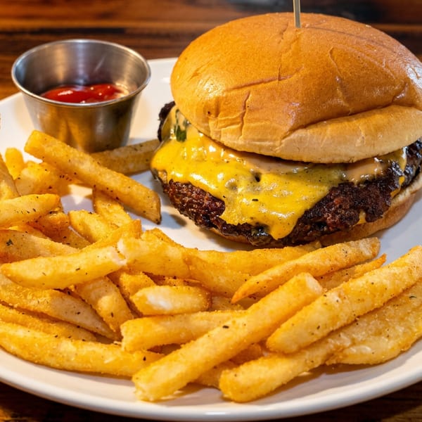 Cheeseburger with melted cheese and special sauce, served with a side of seasoned fries and ketchup.