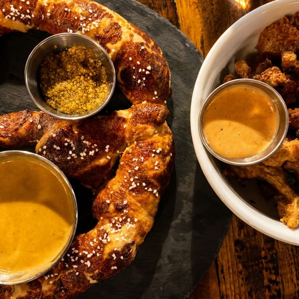 A large pretzel with two dipping sauces and a bowl of fried mushrooms with a dipping sauce.