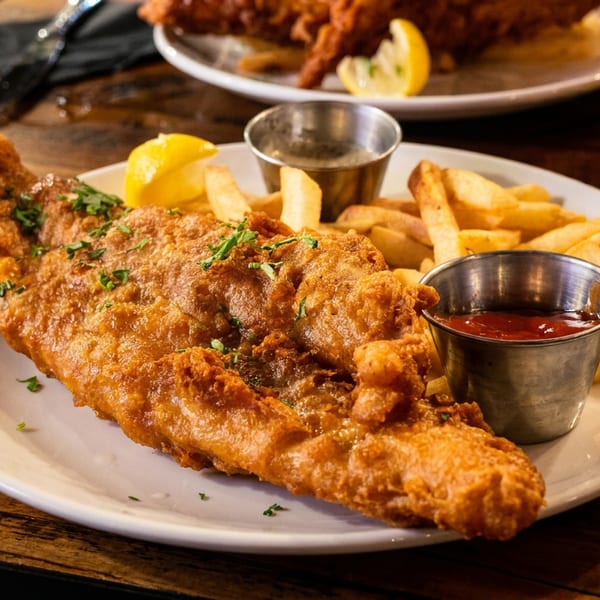 Golden-brown fish and chips with lemon wedges and dipping sauces on a white plate.