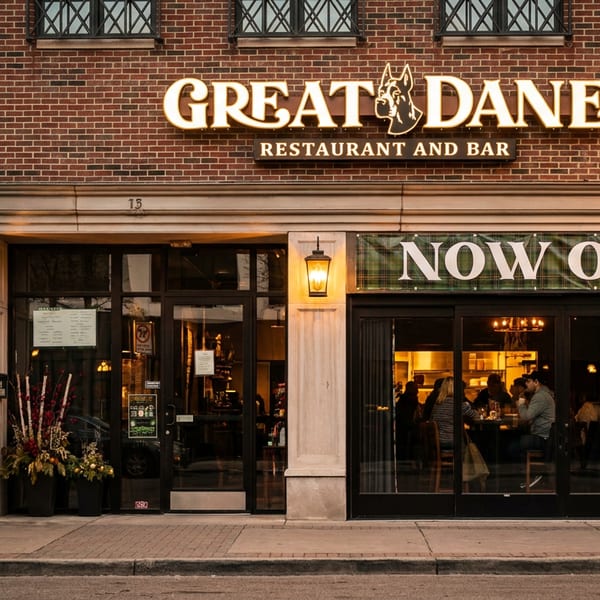 The Great Dane Restaurant and Bar storefront at dusk, with a "Now Open" banner and patrons visible inside.
