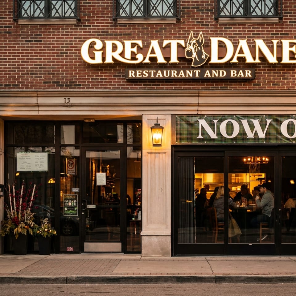 The Great Dane Restaurant and Bar storefront at dusk, with a "Now Open" banner and patrons visible inside.