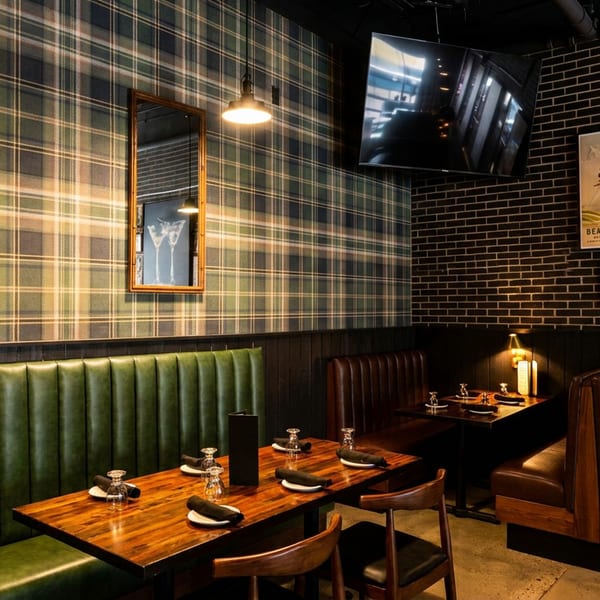 Restaurant interior with green and brown booths, plaid wallpaper, brick wall, and framed artwork.